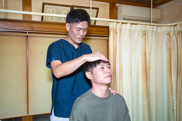 施術前の状態検査の様子、院長が患者様の肩と額のあたりに手を当てている